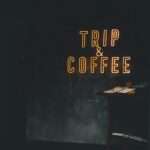 Neon 'Trip & Coffee' sign in a dimly lit café creates a warm, cozy atmosphere.